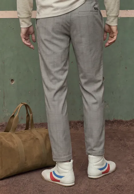 Person von hinten in grauen Hosen und weißen Sneakers mit roten und blauen Streifen, grüne Tasche am Boden.