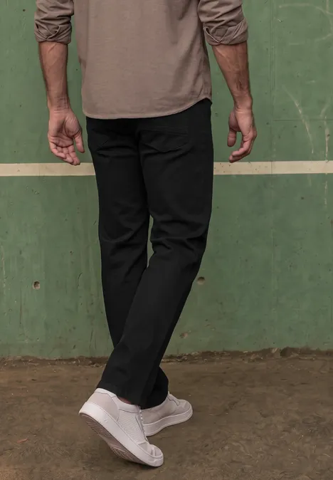 Dżinsy Slim Leg o kroju Slim Fit clean black Dolna część ciała osoby w czarnych spodniach i białych trampkach na tle zielonej ściany.
