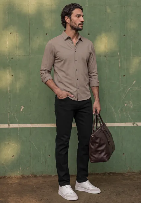 Dżinsy Slim Leg o kroju Slim Fit clean black Mężczyzna w beżowej koszuli, czarnych spodniach i białych trampkach trzyma brązową torbę przed zieloną ścianą.