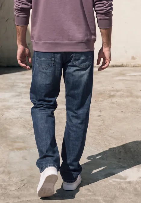Een man loopt weg met een blauwe spijkerbroek, witte sneakers en een paarse trui.