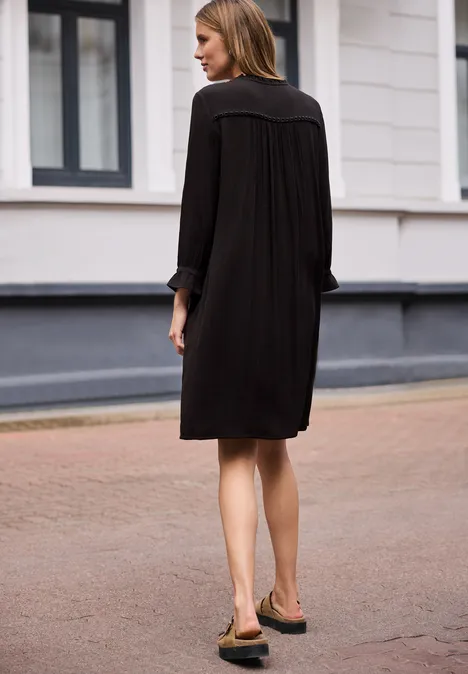 Vrouw van achteren in los zwart jurkje lopend op een geplaveide straat.