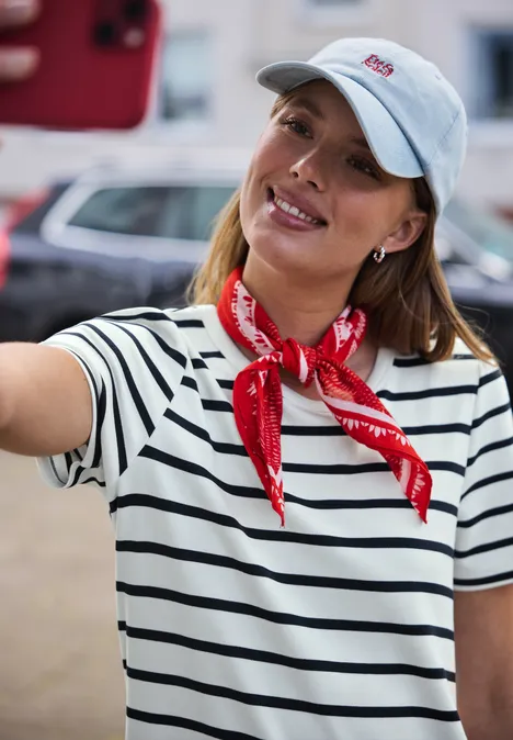 Iemand in een gestreept shirt met rode bandana maakt buiten een selfie met een rode smartphone.