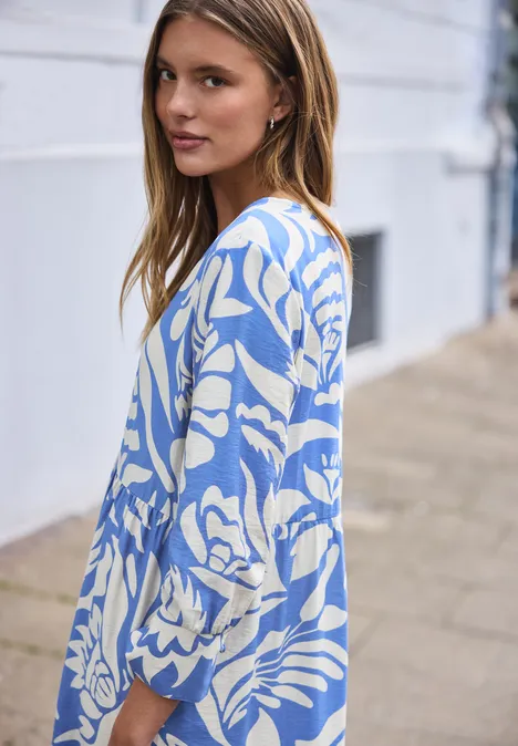 Eine Frau mit langem Haar trägt einen blau-weißen Cardigan mit Blumenmuster auf dem Gehweg.
