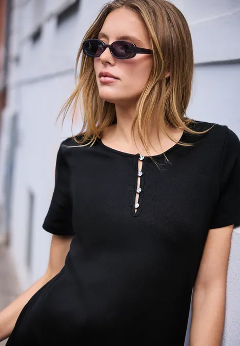 Jonge vrouw in zwart shirt leunt ontspannen tegen een lichte muur, gezicht onscherp.