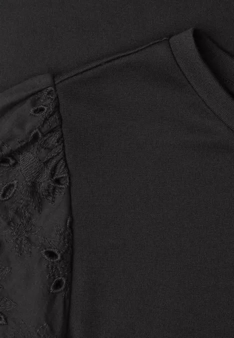 Schwarzes T-Shirt mit Spitze und Ösen am Schulterbereich.