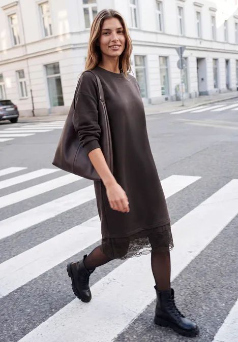 Minikleid mit Spitzendetail am Saum charred brown Eine Frau in dunkelgrauem Kleid mit Spitzenrand, Leggings und schwarzen Boots überquert entspannt einen Zebrastreifen in der Stadt.