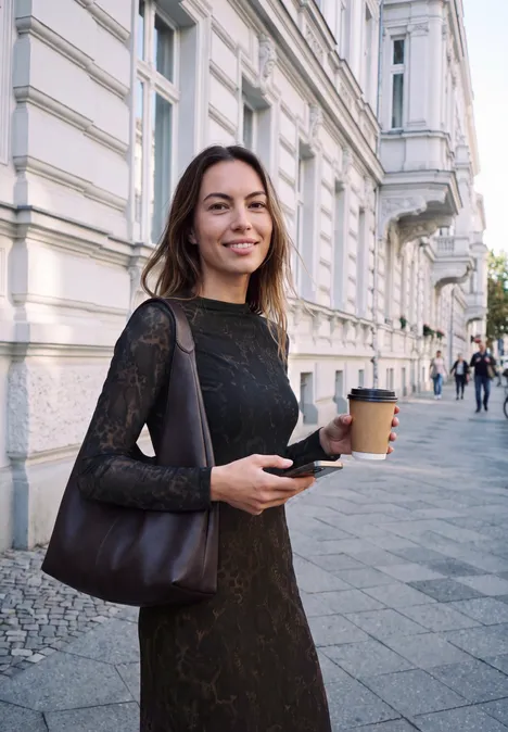 Midikleid aus Mesh mit Snake-Print charred brown Frau in schwarzem Spitzenkleid mit Ledertasche lächelnd auf Straße, hält Kaffee und Handy
