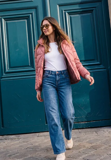 Kurze Jacke mit Stehkragen und Steppmuster Dark Vintage Rose Eine Frau in rosa Jacke und Jeans mit Sonnenbrille spaziert vor einer blauen Tür.