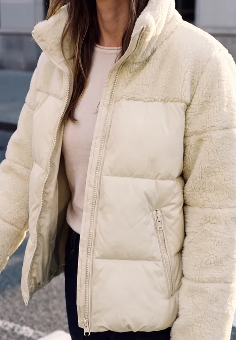 Gros plan sur une veste matelassée crème avec détails en fourrure synthétique.