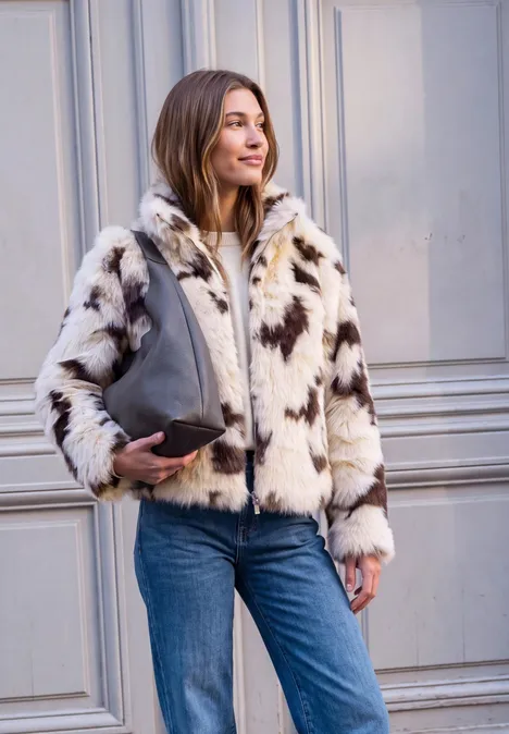 Femme en jean et veste en fausse fourrure beige à motifs, tenant un sac devant des portes claires.