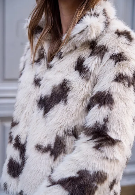 Veste en fausse fourrure blanche à capuche ornée de motifs cœur brun foncé.