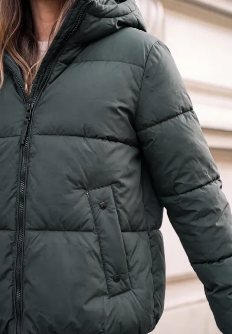 Person trägt eine dunkelgrüne Daunenjacke mit Reißverschluss und seitlichen Taschen im Nahaufnahme.