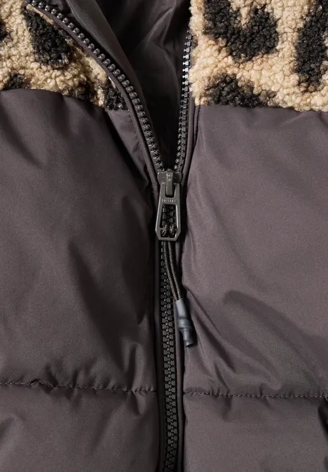 Gros plan d’une veste matelassée avec fermeture éclair noire et doublure moumoute beige tachetée de noir.