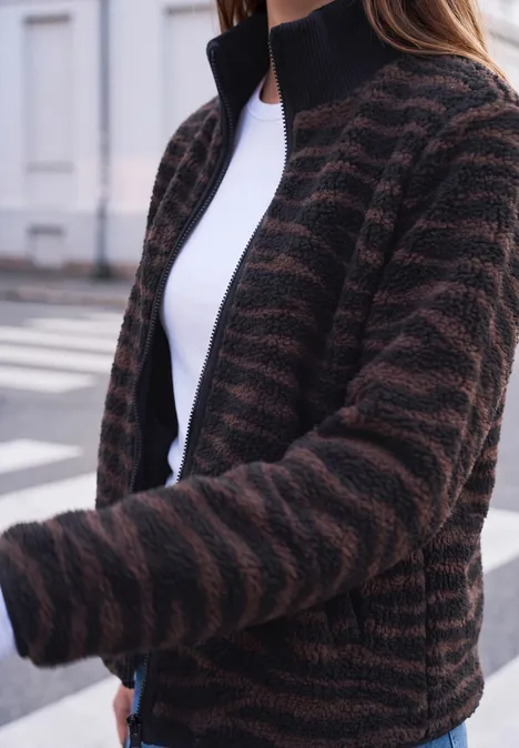 Femme portant une veste polaire rayée brun et noir, col montant, tee-shirt blanc dessous.