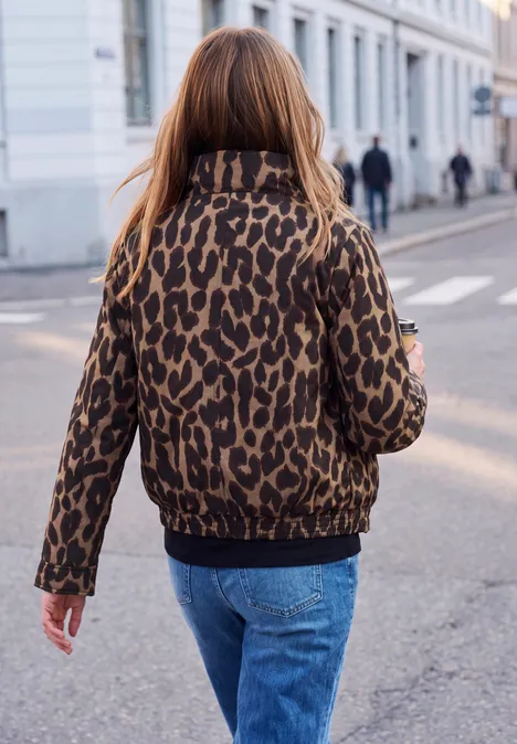 Eine Person in Jeans und brauner Leopardjacke geht die Straße entlang.