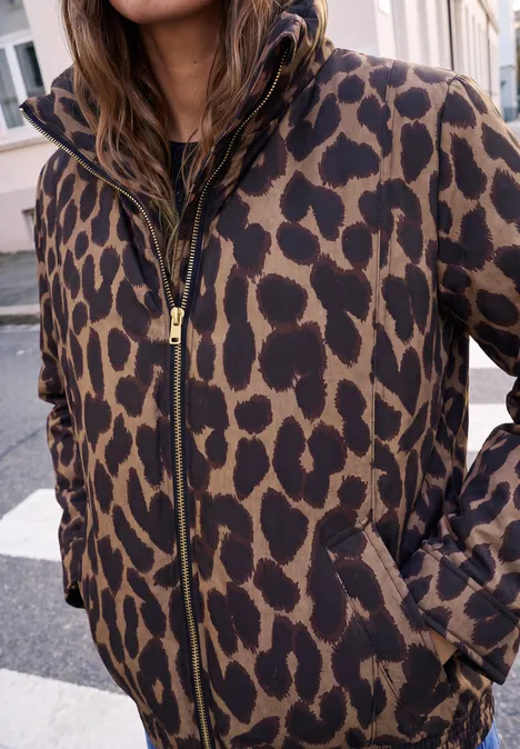 Person trägt eine Kapuzenjacke mit braun-schwarzem Leopardenmuster, Reißverschluss und Taschen.