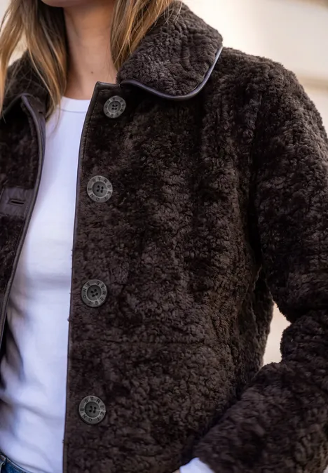 Kobieta ma brązowy, miękki płaszcz typu teddy z guzikami na białej koszulce.