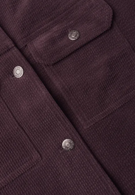 Gros plan sur une veste texturée bordeaux foncé avec boutons-pression argentés et poches plaquées.