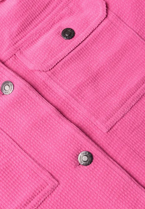Nahaufnahme eines pinken Stoffes mit aufgesetzten Taschen und silbernen Druckknöpfen.