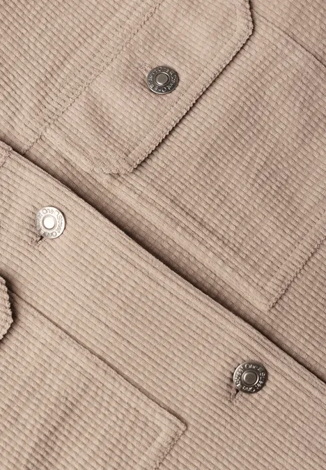 Nahaufnahme einer beige strukturierten Jacke mit aufgesetzten Taschen und silbernen Druckknöpfen.