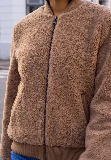 Person trägt eine braune Teddy-Fleecejacke mit Reißverschluss und seitlichen Taschen.