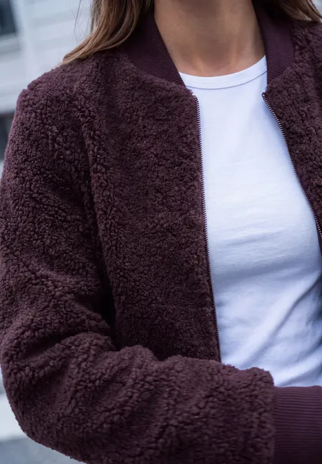 Teddyblouson mit Reißverschluss russet red Eine Person trägt im Freien eine dunkelbraune Teddy-Jacke und ein weißes T-Shirt.