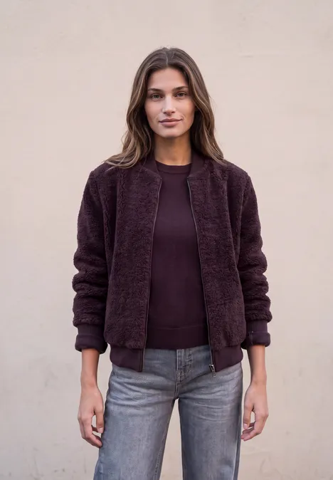 Kurzer Teddyblouson mit Reißverschluss russet red Frau trägt eine dunkelviolette, flauschige Jacke und Jeans vor neutralem Hintergrund.