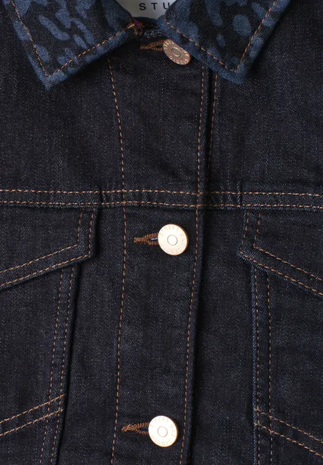 Nahaufnahme einer blauen Jeansjacke mit kontrastierenden orangefarbenen Nähten und hellen Knöpfen.