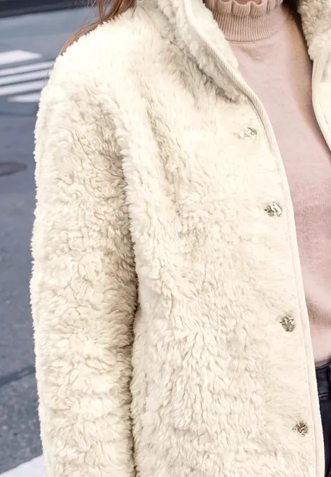 Person trägt eine cremefarbene Teddyjacke mit Druckknöpfen und einen rosafarbenen Rollkragenpullover.