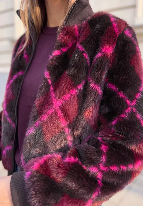 Person trägt rosa-braune Karojacke aus Kunstfell über violettem Pullover.