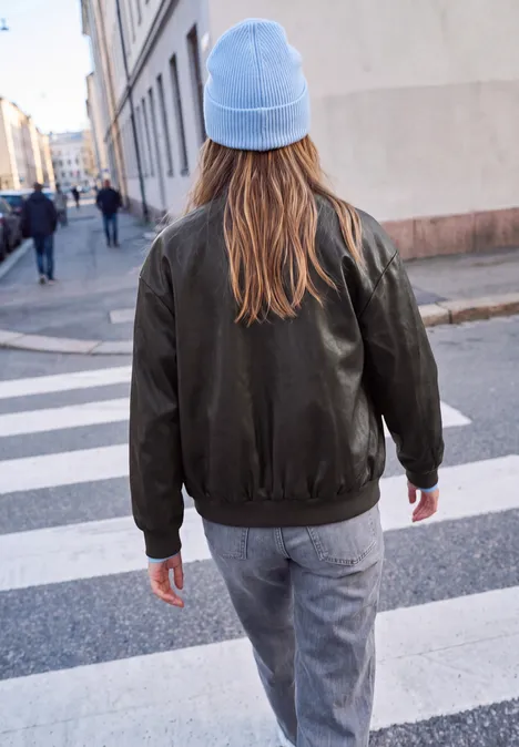 Blouson aspect cuir charred brown Eine Person mit blauer Mütze und grüner Jacke geht über einen Zebrastreifen in einer Stadt.