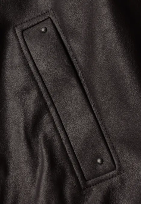 Blouson aspect cuir charred brown Nahaufnahme einer schwarzen Lederoberfläche mit einem eingenähten Riemen und zwei Nieten.