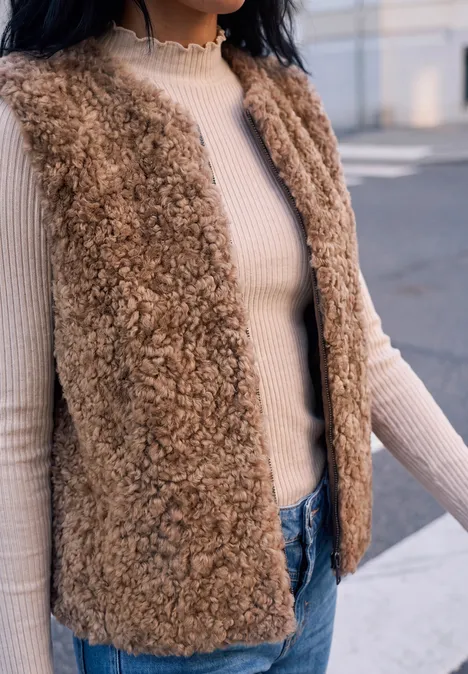 Frau trägt cremefarbenen Rollkragenpullover und flauschige braune Teddyweste.