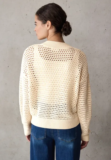 Vrouw met crèmekleurige gebreide trui en spijkerbroek voor grijze muur.