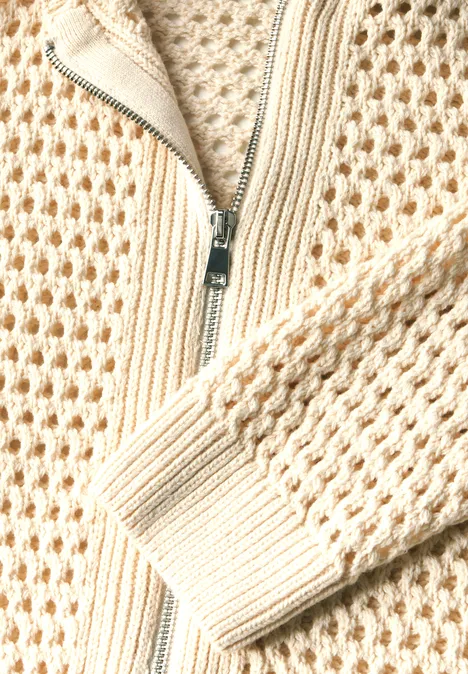 Close-up van een beige gebreid vest met rits.