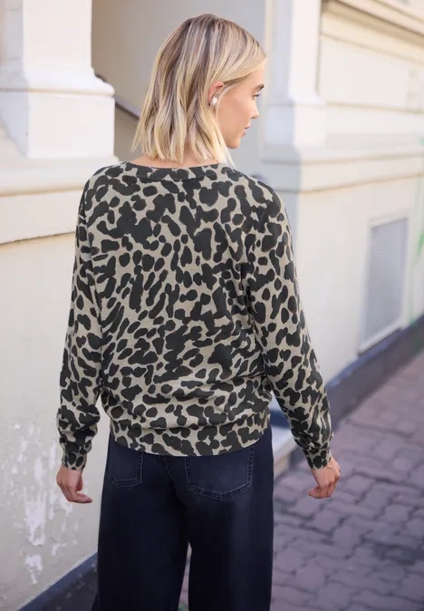 Vest met ronde hals en print light biscuit sand mel. Vrouw van achteren in groene trui met zwart luipaardmotief en donkere spijkerbroek lopend op het trottoir.