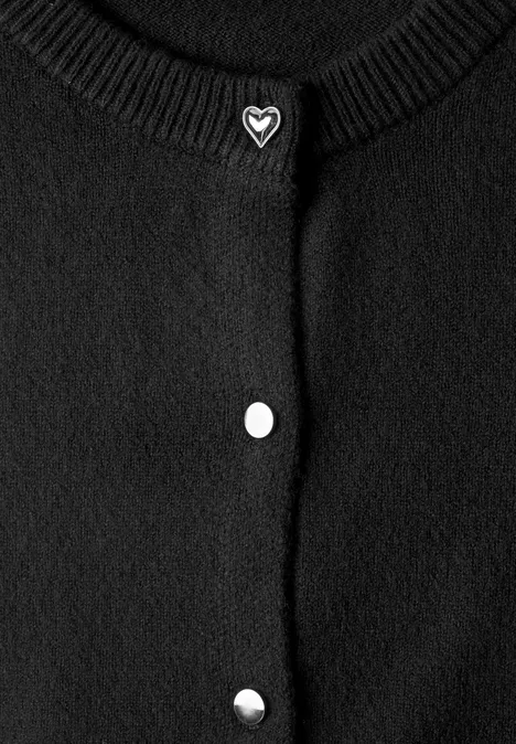 Schwarze Strickjacke mit Rundhalsausschnitt, drei silberne Druckknöpfe und herzförmiger Brosche am Kragen.