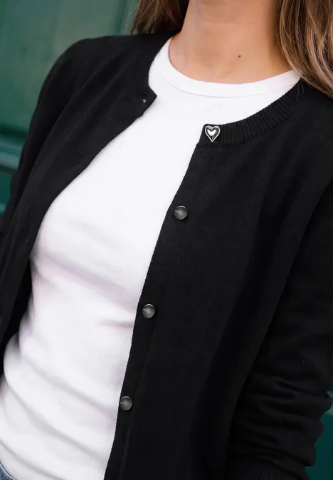 Eine Person trägt ein weißes T-Shirt unter einer schwarzen Strickjacke mit Knöpfen.
