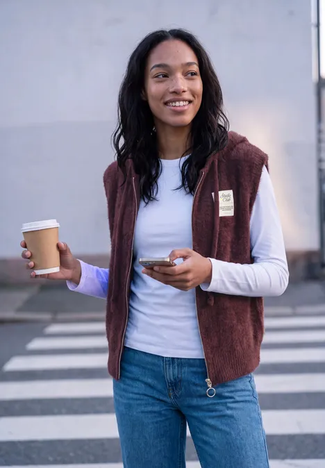 Weste mit Kapuze und Zipper very berry Frau mit Kaffee und Smartphone in der Hand steht auf einem Zebrastreifen.
