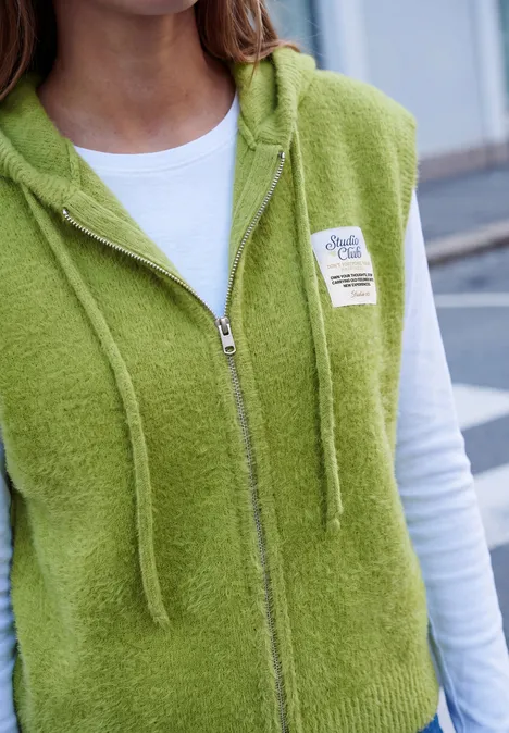 Persoon draagt een lichtgroene, zachte zip-up hoodie over een wit shirt.