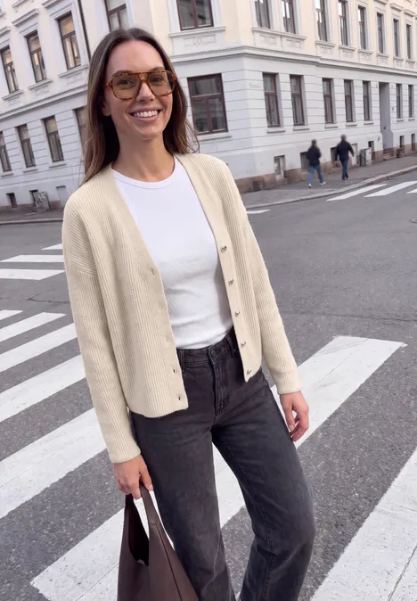 Cardigan mit V-Neck und Knopfleiste creamed sand mel. Junge Frau in Cardigan, weißem Shirt und Jeans mit Tasche an einem Zebrastreifen in der Stadt.