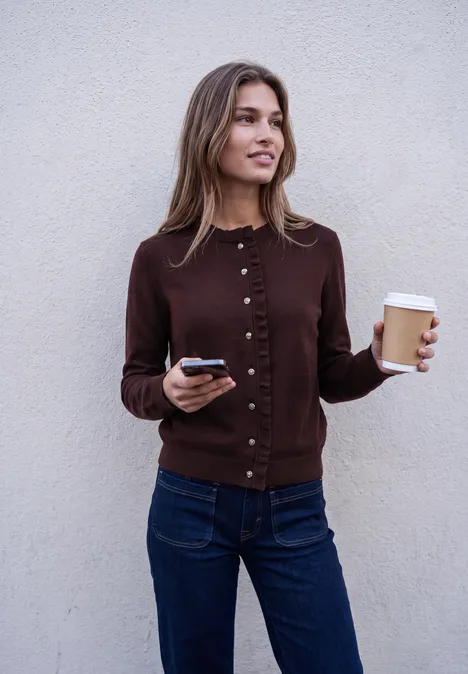 Cardigan mit Rundhals und Rüschendetails russet red Eine lächelnde Frau hält einen Kaffeebecher und ein Handy vor einer hellen Wand