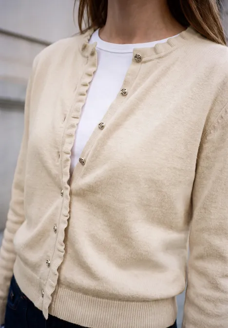 Cardigan mit Rundhals und Rüschendetails creamed sand mel. Eine Frau trägt eine beige Strickjacke über einem weißen Shirt, teilweise geöffnet.