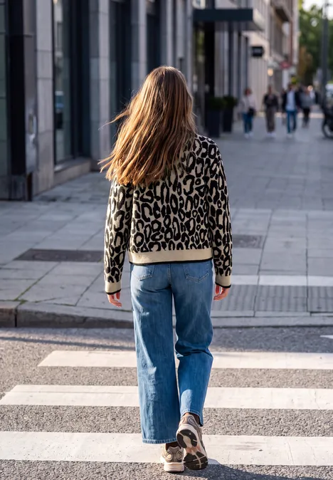 Cardigan mit Leo-Muster und Zipper biscuit sand mel. Eine Person mit Leopardenjacke und Jeans geht über einen Zebrastreifen auf einer Stadtstraße.