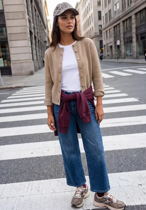 Cardigan à côtes et col rond biscuit sand mel. Junge Frau im lässigen Outfit und Cap läuft über Zebrastreifen