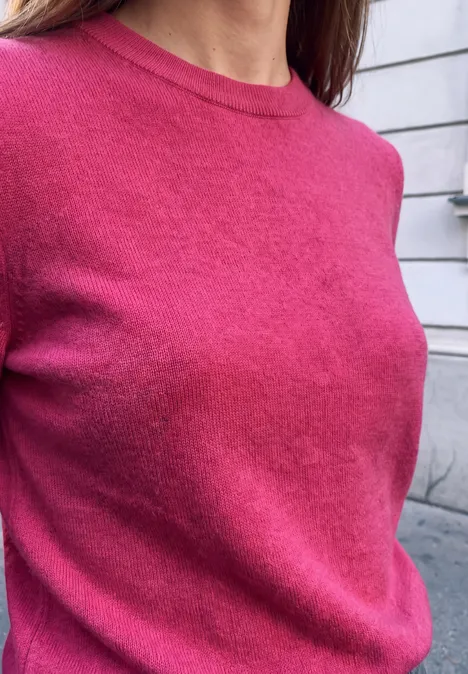 Pullover mit Rundhals in Unifarbe ruby raspberry mel. Nahaufnahme eines Oberkörpers in einem pinken Pullover vor einer hellen Wand.