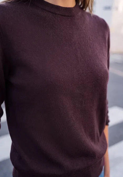 Nahaufnahme einer Person in dunkelrotem Pullover, nur Oberkörper, urbaner Hintergrund.