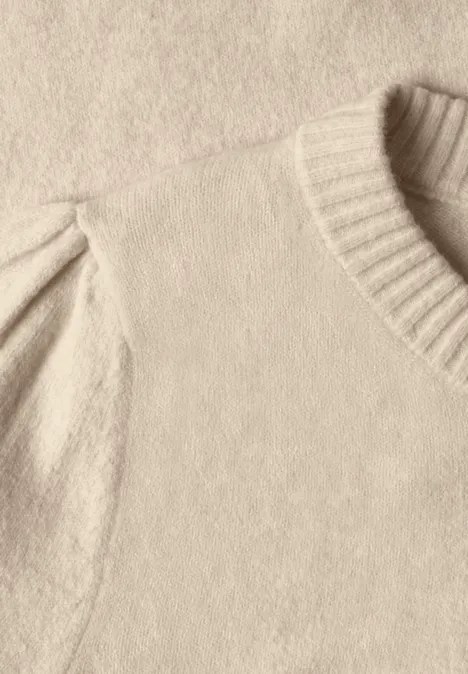 Nahaufnahme eines cremefarbenen Strickpullovers mit geripptem Rundhalsausschnitt und leicht gepufften Ärmeln.