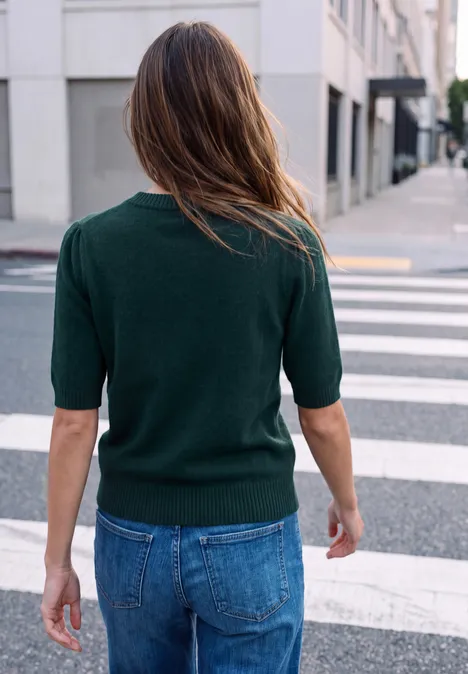 Person in grünem Pullover und Jeans läuft über einen Zebrastreifen in der Stadt.