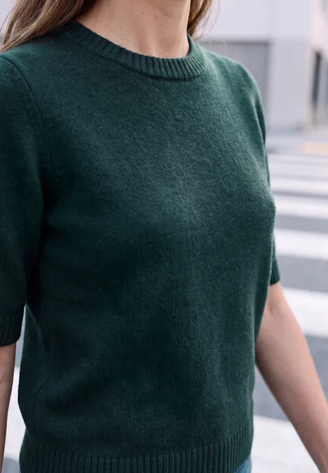 Person trägt dunkelgrünen Kurzarm-Strickpullover, stehend auf einem Zebrastreifen.